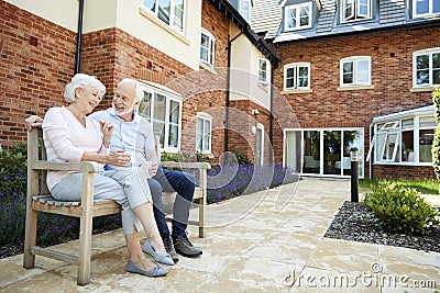 Retired Couple Sitting On Bench With Hot Drink In Assisted Living Facility Stock Photo