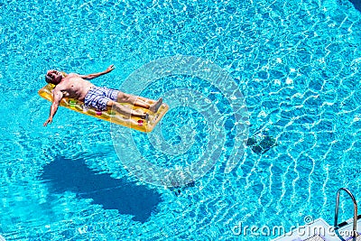 Retired lifestyle beautiful man senior age relaxing and enjoying the blue water pool sleeping on a orange coloured trendy lilo in Stock Photo