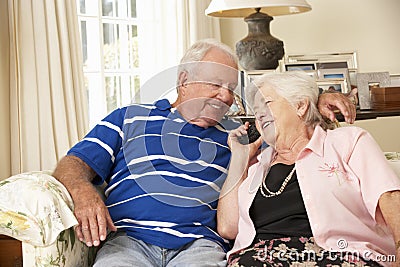 Retired Senior Couple Sitting On Sofa Talking On Phone At Home Together Stock Photo