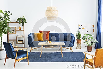 Retro armchairs with wooden frame and colorful pillows on a navy blue sofa in a vibrant living room interior with green plants. Re Stock Photo