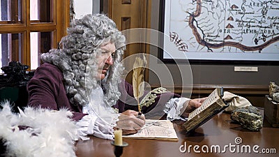 Retro baroque man with white wig holding a quill pen, sitting at antique table and thinking about paper documents Stock Photo