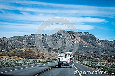 Retro camper mounted on pickup truck with smoke blowing out the back drives down two lane highway through sagebrush to badlands Editorial Stock Photo