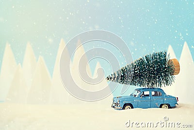 Retro car toy carrying Christmas fir tree in snowy landscape. Christmas or New Year celebration concept. Copy space. Selective Stock Photo