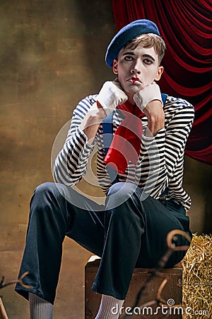 Vintage portrait of male mime artist expressing sadness and loneliness over dark retro circus backstage background Stock Photo