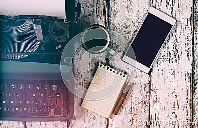 Retro filtered image of vintage typewriter, blank notebook, cup of coffee and smartphone on wooden table Stock Photo