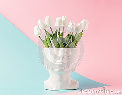 Retro head sculpture with tulip flowers on a pastel blue pink background. Stock Photo