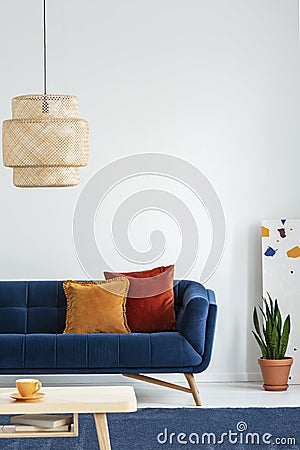 Retro lampshade above a simple, wooden coffee table on a navy blue rug in a colorful living room interior with pillows on a couch. Stock Photo