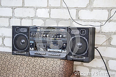 Retro portable radio stereo cassette player. Boombox lays outside on the sofa against the white wall from bricks background. Old Stock Photo