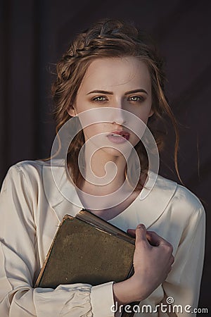 Retro portrait of a beautiful dreamy girl holding a book in hands outdoors. Soft vintage toning. Stock Photo