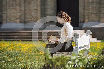 Retro portrait of a beautiful dreamy girl reading a book outdoors. Soft vintage toning. Stock Photo