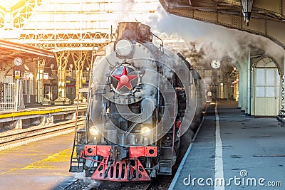 Retro steam train stands on the vintage railway station. Stock Photo