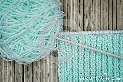 Retro-style photo of a woolen yarnroll, knitting needles, and knitwork in progress on wooden background Stock Photo