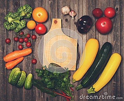 Retro styled vintage food background. Fresh vegetables and ingredients for cooking around cutting board on rustic weathered wood Stock Photo