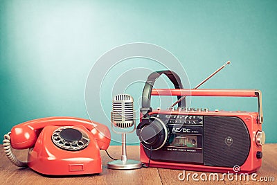 Retro telephone, radio and cassette player, headphones, microphone on table front mint blue background. Vintage style photo Stock Photo