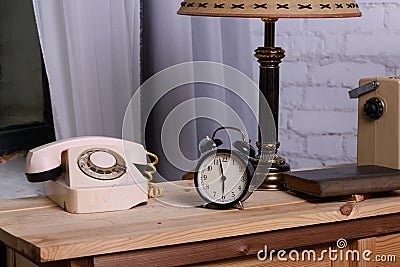 Retro things on table, close upRetro things on table, close up. An old dial phone, a black alarm clock, a table lamp, a book, and Stock Photo