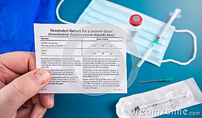 Return for a second dose card with facial mask, covid-19 vaccine vial and syringe on blue Stock Photo