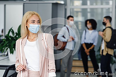 Return to work after lockdown and new normal. Woman in protective mask looks to the side in corridor of modern office Stock Photo