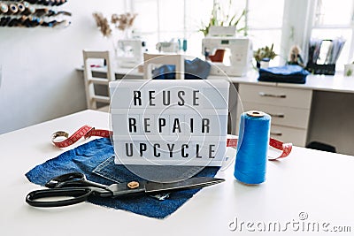 Reuse, repair, upcycle text on light board on sewing machines background. Stack of old jeans, Denim clothes, scissors Stock Photo