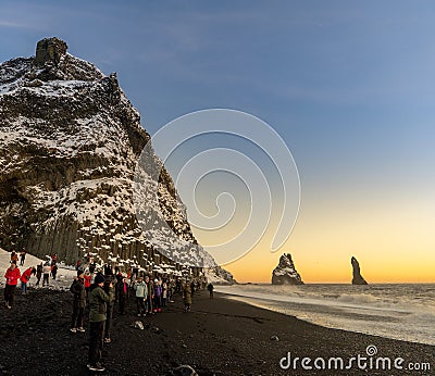 Reynisfjara black sand beach at sunset and the basalt formations covered in snow and illuminated by the last rays of the sun from Editorial Stock Photo