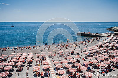 Rhythm of red umbrellas and tourists on a sunny beach in Genoa, Italy. Stock Photo