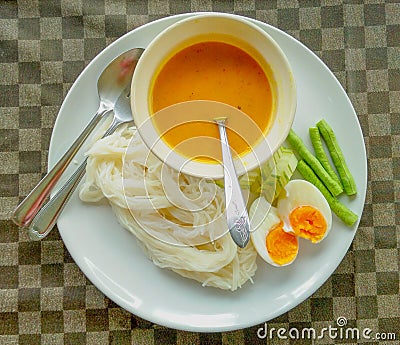 Rice noodle curry with spices and fish Boiled eggs cut in half, long pods, cucumbers, sliced on a white plate Is another popular Stock Photo