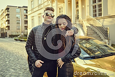 A rich couple near their cottage, and their expensive golden car. A man came to a party with a girl. Couple in black, fashion phot Stock Photo