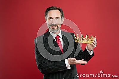 Rich reward. Mature businessman showing crown reward on red background. Successfil big boss awarding winner with Stock Photo