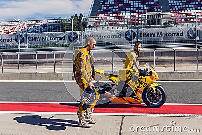 Rider yellow suit and helmet, and technical personnel to carry the bike around the pits after the race Editorial Stock Photo
