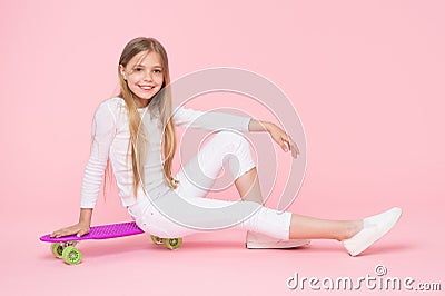 Riding board in style for years to come. Happy little child sitting on board deck on pink background. Cute small skater Stock Photo