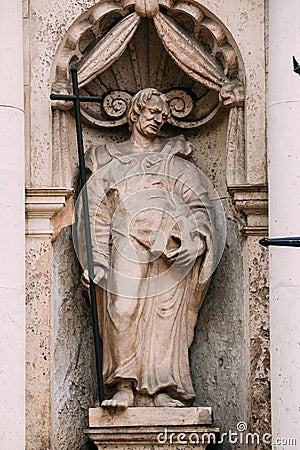 Riga Latvia. Close Ancient Statue Of Man With Cross And Book In Hands On The Facade Of St. Peter Church, Stock Photo