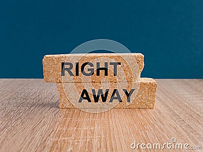 RIGHT AWAY ?oncept. The text RIGHT AWAY is written on a brick blocks. Beautiful wooden table, dark blue background background. Stock Photo