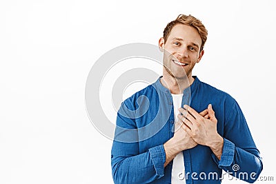 Right into my heart. Smiling attractive ginger guy holding hands on heart, being touched and happy, flattered by nice Stock Photo