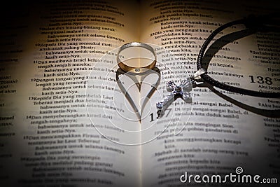 ring with heart shadow and cross necklace symbol of love and christianity between indonesia language Holy Bible page Stock Photo
