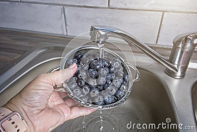 Rinsing blueberries in a stainless steel colander under running water Stock Photo