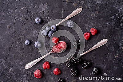 Ripe blueberries, raspberries, blackberries, Mixed berries with three spoons. Various fresh summer berries on dark solid backgroun Stock Photo