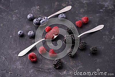 Ripe blueberries, raspberries, blackberries, Mixed berries with three spoons. Various fresh summer berries on dark solid backgroun Stock Photo