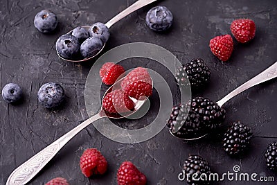 Ripe blueberries, raspberries, blackberries, Mixed berries with three spoons. Various fresh summer berries on dark solid backgroun Stock Photo