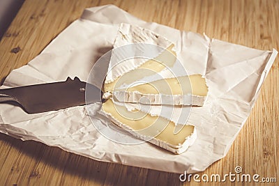 Ripe brie cheese cut into slices on paper with mouse shaped knife Stock Photo