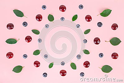 Ripe cherries, blueberries and green leaves arranged in a circle on a pink background Stock Photo