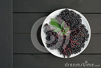 Ripe elderberry in plate on wooden black background Stock Photo