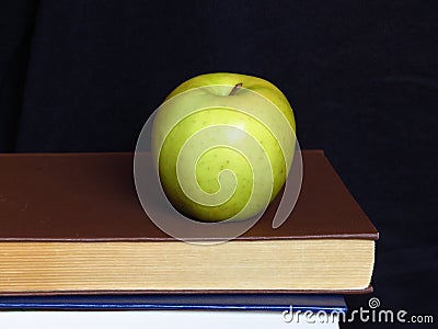 A ripe green isolated apple on book pile on black background. Stock Photo