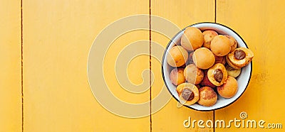 Ripe juicy homemade apricots with cracks and flaws in the plate and scattered on a bright yellow wooden surface. Harvest banner Stock Photo