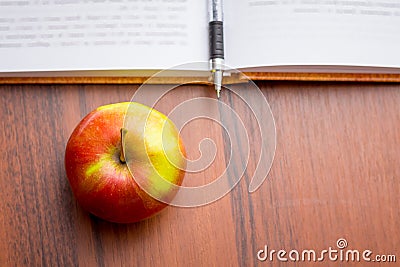 Ripe juicy red apple near the book and pen. Useful food during a Stock Photo