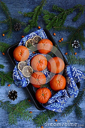 Ripe, juicy tangerines on a blue napkin, orange sea buckthorn berries, fir branches and cones on a blue background Stock Photo