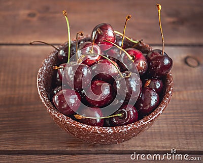 Ripe large sweet cherries in a deep ceramic brown bowl on an wooden tray Stock Photo