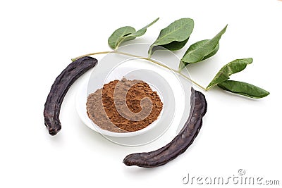 Ripe organic carob fruit pods, green leaves from locust tree and carob powder in plate on white background. Healthy alternative to Stock Photo