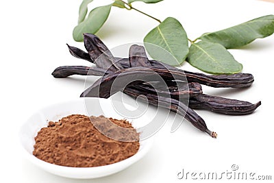 Ripe organic carob fruit pods with green leaves from locust tree and carob powder on white background. Healthy alternative to Stock Photo