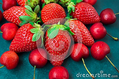 Ripe organic strawberries, glossy sweet cherries arranged in form of flower, blue background, styled creative image, closeup Stock Photo