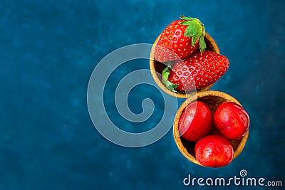 Ripe organic strawberries glossy sweet cherries in waffle ice cream cones, dark blue background, template Stock Photo