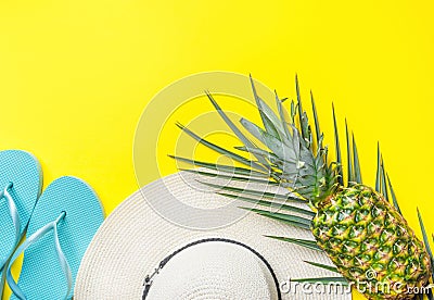 Ripe pineapple on green palm leaf white straw hat blue slippers on bright yellow solid background. Summer vacation fun Stock Photo